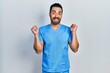 © Krakenimages.com - Handsome hispanic man with beard wearing blue male nurse uniform celebrating surprised and amazed for success with arms raised and open eyes. winner concept.