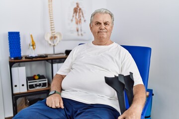 Sticker - Senior caucasian man at physiotherapy clinic holding crutches with a happy and cool smile on face. lucky person.