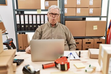 Sticker - Senior caucasian man working at small business ecommerce with laptop making fish face with lips, crazy and comical gesture. funny expression.