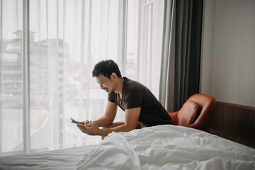 Wall Mural - Asian man feels happy with his phone result while on vacation in the hotel.