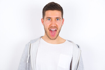 Wall Mural - young caucasian man wearing casual clothes over white background with happy and funny face smiling and showing tongue.