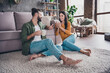 © deagreez - Portrait of attractive cute cheerful couple sitting on floor carpet communicating spending day drinking cacao at home house flat indoors