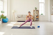 © Studio Romantic - Female fitness trainer performs sports exercises in front of webcam doing streaming workout for her class. Girl training on sports mat in living room. Concept of online recording of fitness tutorial.