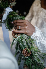 Wall Mural - Bouquet of flowers in the hand of the African American bride Greenery with Conifer cone bouquet in bride's hands Close up Diamond ring on her finger Cropped photo	