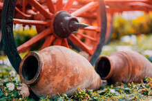 Old ceramic jugs next to red cart wheel in a garden decoration in Turkey.