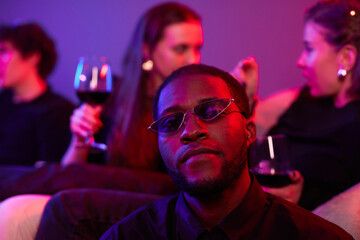 Wall Mural - Close up of African American man wearing colored sunglasses at party lit by neon lights