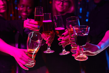 Close up group of women holding champagne glasses to camera while partying in neon light