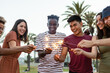 © Xavier Lorenzo - Happy young friends having fun holding sparkles at festival eve - Diverse group of multiracial people celebrating together on summer outdoors party