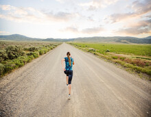 United States, Utah, Cedar Fort, Rear View Of Woman Jogging On Road In Desert Landscape