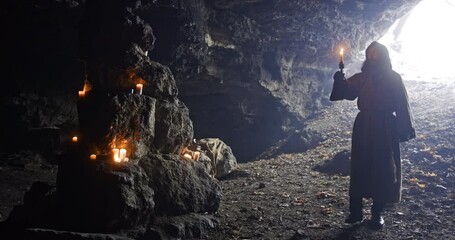 Wall Mural - friar with a candle in his hands wanders in a large dark cave on a background of lighted candles