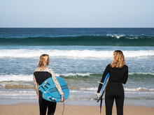 Unrecognizable Surfer Females On The Beach Shore Watching The Waves