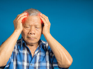 Senior man suffering headache pain while standing against a blue background