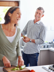 Wall Mural - Making each other laugh. Shot of a mature couple laughing while preparing a meal together in the kitchen.