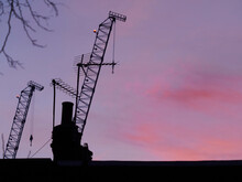 A Vibrant, Rich Dawn Over London, With Cranes, Chimney Pots And Aerials Silhouetted Against A Purple, Pink And Red Sky.