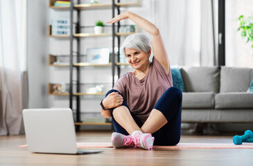 Wall Mural - sport, fitness and healthy lifestyle concept - smiling senior woman exercising with laptop computer on mat at home