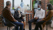 © DC Studio - Therapist giving advice to multi ethnic group of people with face mask at aa meeting. Woman counselor talking to patients about addiction at therapy session during coronavirus pandemic.