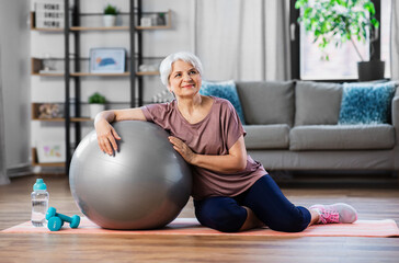 Wall Mural - sport, fitness and healthy lifestyle concept - smiling senior woman with exercise ball sitting on mat at home