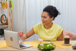 © kinomaster - Cute African American woman talking by video call on a laptop. A young woman demonstrates a painted egg and Easter cake while sitting at a decorated holiday table. Happy easter. Close up.