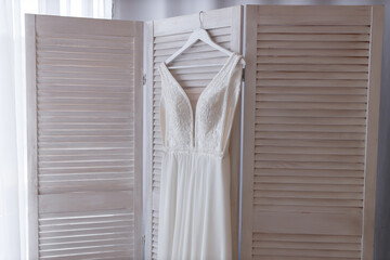 Wall Mural - Classic wedding long white sleeveless dress on a hanger hanging on a wooden screen