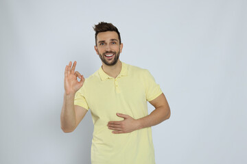 Wall Mural - Happy man touching his belly and showing okay gesture on light background. Concept of healthy stomach