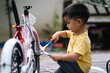 Cute asian little toddler boy is trying help father to assemble new bicycle by himself, concept of learning, practice and practical life skill for kid education and development at home in family life.
