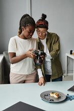 Vertical Portrait Of Two Female Photographers Looking At Photos In Camera While Working At Photo Studio