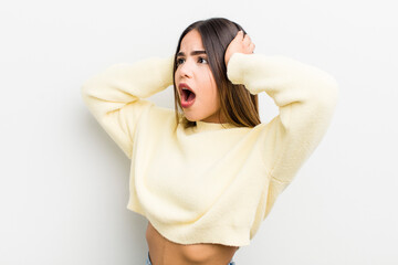 pretty hispanic woman with open mouth, looking horrified and shocked because of a terrible mistake, raising hands to head