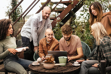 six gen z Erasmus students from different countries gathering using laptop on a terrace co-working space, studying and discussing about lessons together.