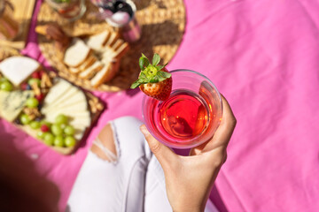 Wall Mural - Horizontal top view of unrecognizable woman drinking a strawberry juice outdoors. Above shot of woman holding a strawberry fruit juice on pink picnic background. Health and drink concept.