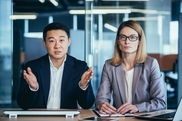 Wall Mural - a team of business employees at an online meeting look at camera and communicate. Webcam view. conference remote interview. Two office workers talking Video call conversation. Asian male and female