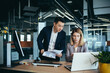 © Liubomir - Two employees in a modern office, an Asian man and a woman working at a table, colleagues discussing and consulting, thinking about a joint project