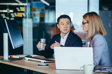 Wall Mural - Two employees are having fun. Asian man and blonde woman taking a break, colleagues working together in a modern office