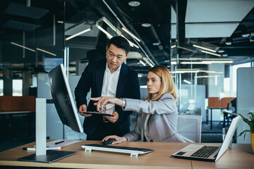 Two Asian male and female colleagues in a modern office, a woman shows the work done on the monitor, consults and discusses