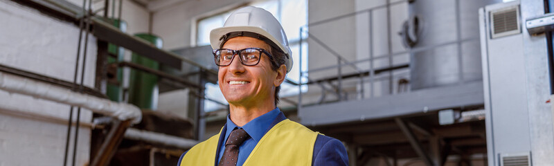 Cheerful matured man in safety helmet looking at camera and smiling while holding folder with papers