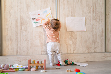 One baby girl back view full length of one infant child standing putting drawing on the wall at home real people copy space family childhood development and growing up concept