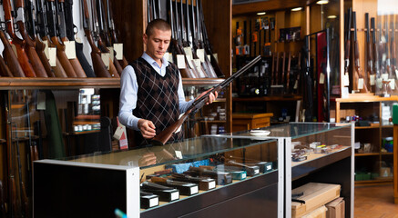 Wall Mural - Adult owner of the gun shop demonstrates a rare collectible hunting rifle