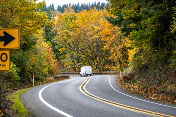 Compact cargo mini van for small business and deliveries running on the winding mountain autumn road with yellow forest in Columbia Gorge area.