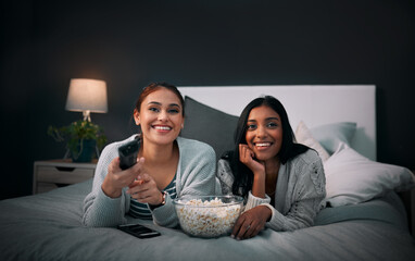 Wall Mural - We have everything we need right here. Shot of two young women eating popcorn while watching a movie at home.