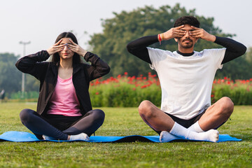 Young couple doing yoga and meditating in the park early in the morning. Healthy lifestyle concept.