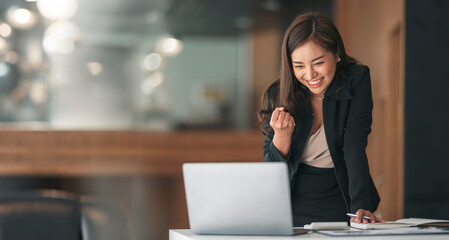 Young successful businesswoman raising her hands up and laughing with happiness.