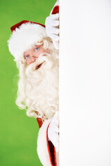 Canvas Print - Peeping Santa. Santa peeking out around the corner of a white wall, on a green background - copyspace.