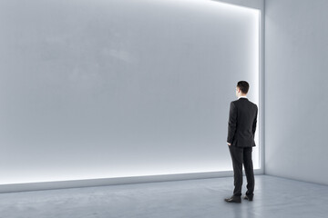 Poster - Man standing in modern exhibition hall interior with illuminated white mock up wall and concrete floor. Gallery concept.