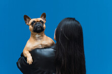 Happy Asian Woman Hugging Dog While Standing On Blue Background