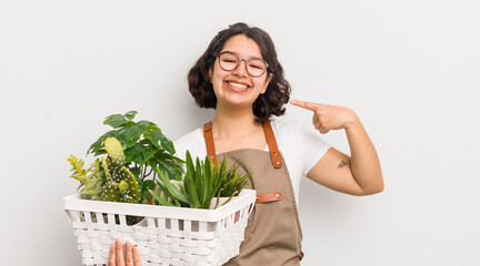 Wall Mural - pretty hispanic girl smiling confidently pointing to own broad smile. plants concept