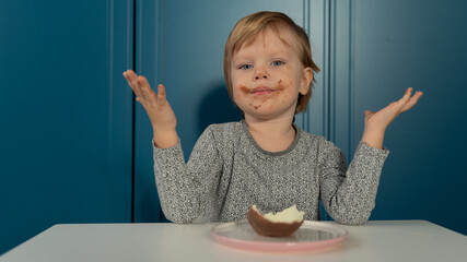 Wall Mural - A boy eats a chocolate egg, all dirty, on a blue background