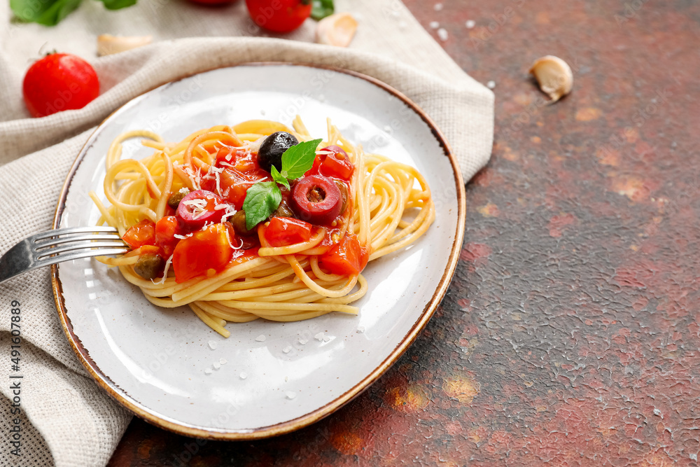 Plate with tasty Pasta Puttanesca on grunge background