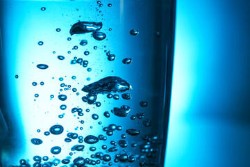 Glass of clear water with bubbles on blue background, closeup