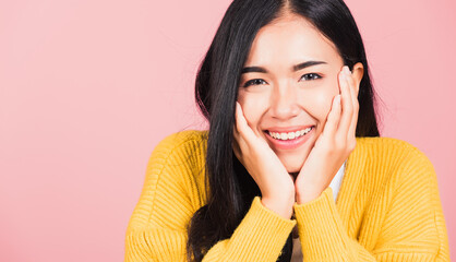 Wall Mural - Happy Asian portrait beautiful cute young woman smile holding her cheeks looking to camera studio shot isolated on pink background Thai female beauty face touch massage healthy skin with copy space