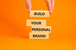 © Dzmitry - Build your personal brand symbol. Concept words Build your personal brand on wooden blocks. Businessman hand. Beautiful orange background. Build your personal brand business concept. Copy space.