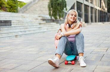 Wall Mural - Young smiling cool girl sitting on skateboard in the city